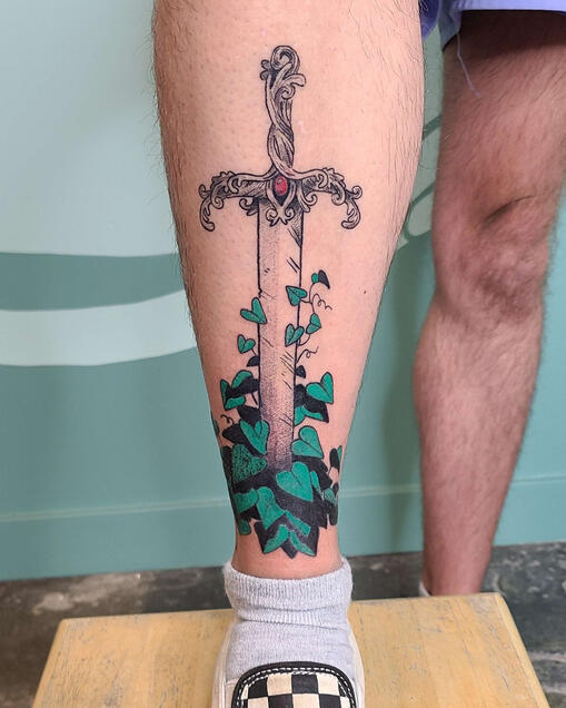 black and green tattoo of a sword with vines growing on it.